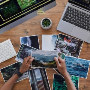 Minimal background composition of male hands holding printed photographs over textured wooden desk, photographers office concept, copy space